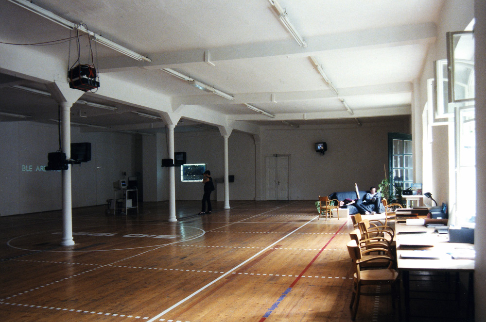 Art, artwork. An installation entitled "Reflex" by Nika Span / Nika Špan. Material: VHS player, VHS cassette (245 minutes), a video projector, a TV stand, a television set, a two-way mirror, an electric motor. Exhibition: SIQ 1999, WUK, Kunsthalle Exnergasse, Vienna, Austria. 