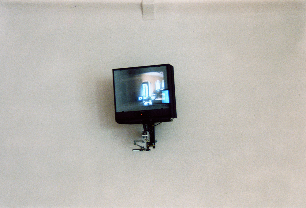 Art, artwork. An installation entitled "Reflex" by Nika Span / Nika Špan. Material: VHS player, VHS cassette (245 minutes), a video projector, a TV stand, a television set, a two-way mirror, an electric motor. Exhibition: SIQ 1999, WUK, Kunsthalle Exnergasse, Vienna, Austria. 