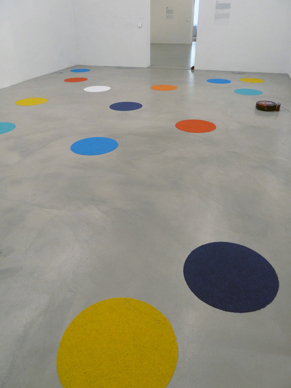 Art, artwork. An installation "Vacuumination" by Nika Span / Nika Špan. Material: A robot vacuum cleaner, coloured gravel. Exhibition: Homeland, MMKK, Klagenfurt, Austria 